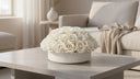Amélie, a dome of cream white preserved roses in a white ceramic bowl, on a stone coffee table in a sunlit living room