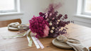 Plum and burgundy preserved hydrangea bouquet laid on a wooden dining table with linen napkins