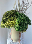 Eden arrangement carried in both hands, bare branches rising above the foliage