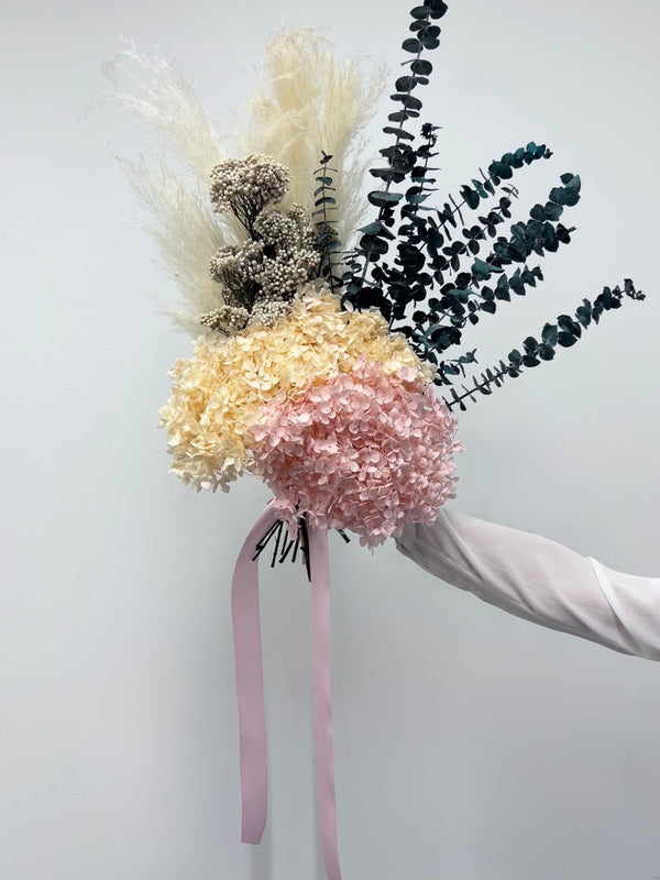 Noelle bouquet of blush and cream preserved hydrangea with dark eucalyptus, held in one hand