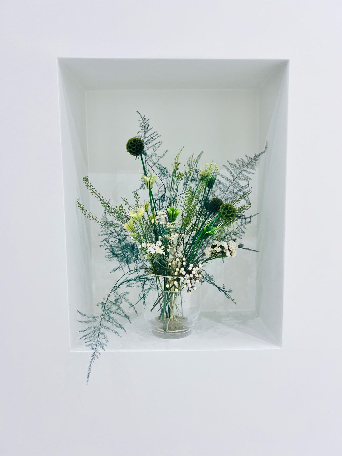 A preserved floral arrangement in a glass vase in a wall niche at Energy Plus