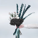 A bouquet of black preserved hydrangea and teal eucalyptus tied with a teal ribbon