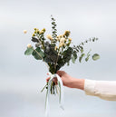 A hand-tied bouquet of preserved eucalyptus with cream and yellow blooms