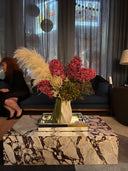 A tall preserved arrangement of red blooms and pampas grass on a marble coffee table in a lounge