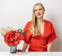 A woman in a red dress beside a vase of red preserved hydrangeas