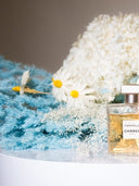 Preserved white hydrangea with daisies and blue grasses beside a perfume bottle