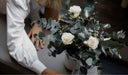 A florist arranging preserved white roses and eucalyptus