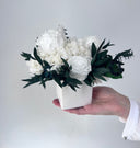 White preserved roses and hydrangea with dark foliage in a square white vase