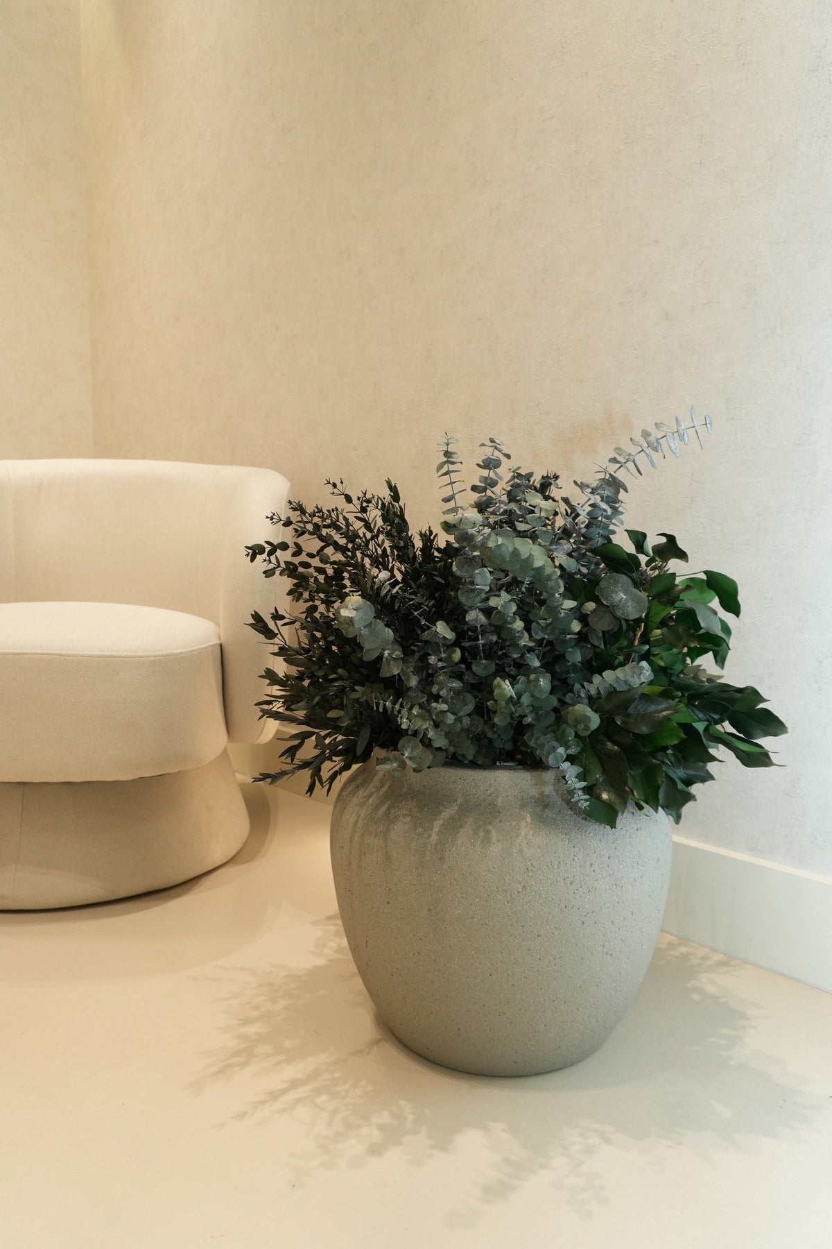 Preserved eucalyptus in a round stone-coloured pot beside a cream armchair at Vivant Mind