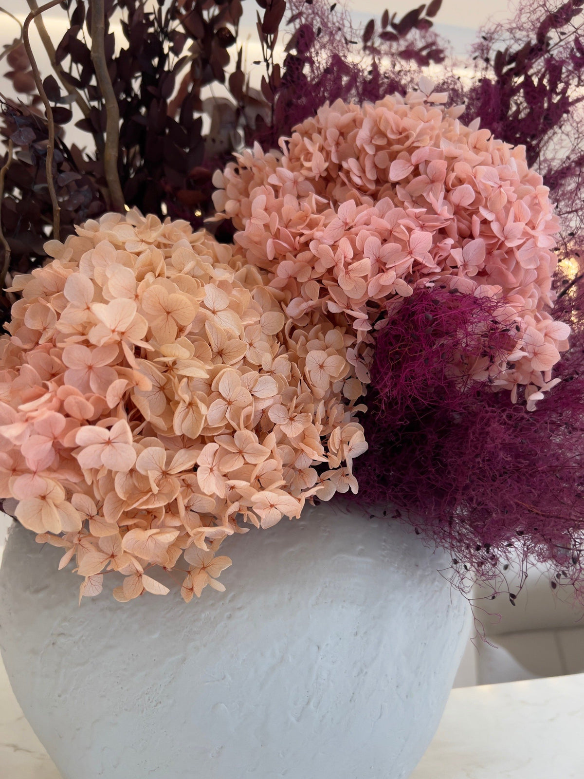 Close-up of preserved peach hydrangea and plum smoke bush in a white textured vase at Vivant Mind
