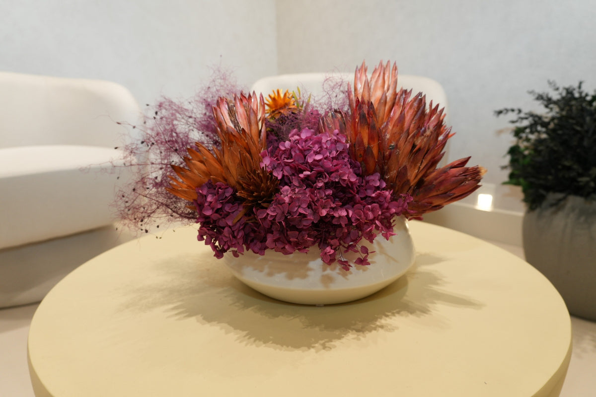 A bowl of preserved protea, magenta hydrangea and dried grasses on a round table between cream chairs at Vivant Mind