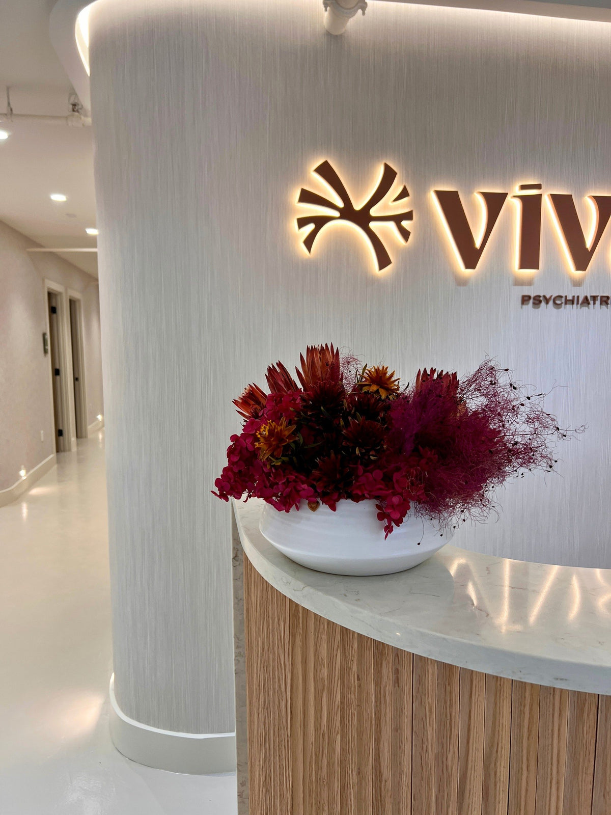 A low bowl of preserved red protea and hydrangea on the curved reception counter under the vivant sign