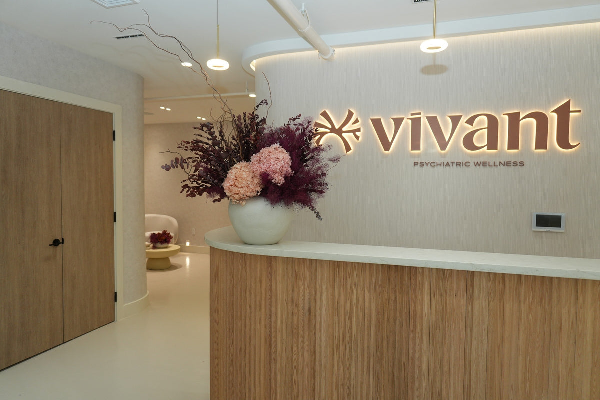 A preserved arrangement of pink hydrangea and plum grasses on the Vivant Mind reception desk, beside the lit vivant sign