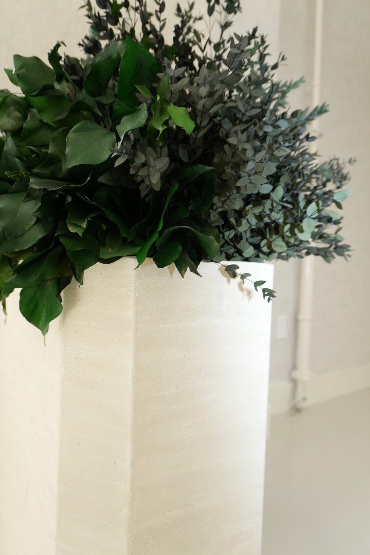 Preserved greenery spilling over a tall cream planter at Vivant Mind
