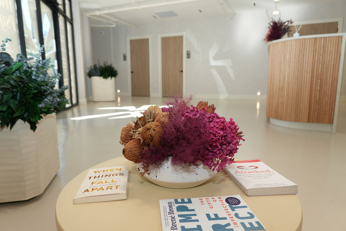 A waiting table with a bowl of preserved flowers and books, the reception desk and planters behind, at Vivant Mind
