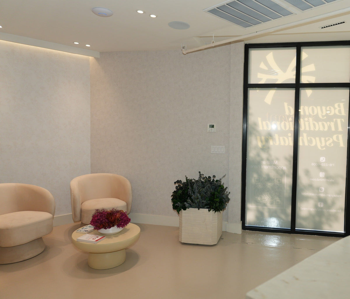 A waiting corner by the Vivant Mind entrance: two cream chairs, a low table with preserved flowers and a planter of preserved foliage