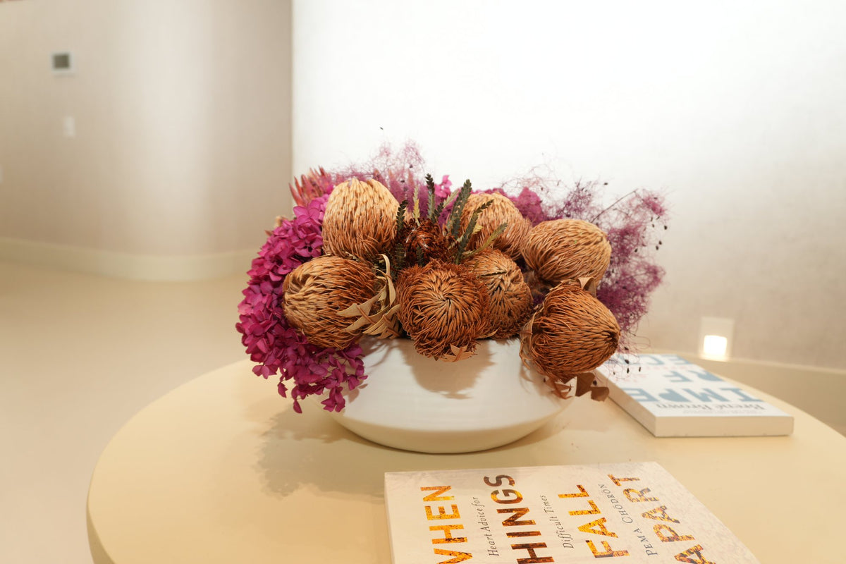 A bowl of preserved protea and magenta hydrangea on a round waiting-room table at Vivant Mind